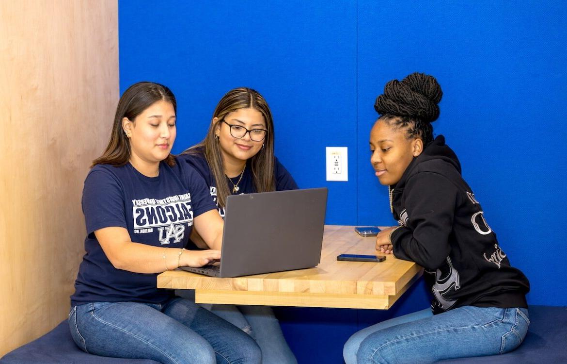 Three students in the student center looking at a laptop.